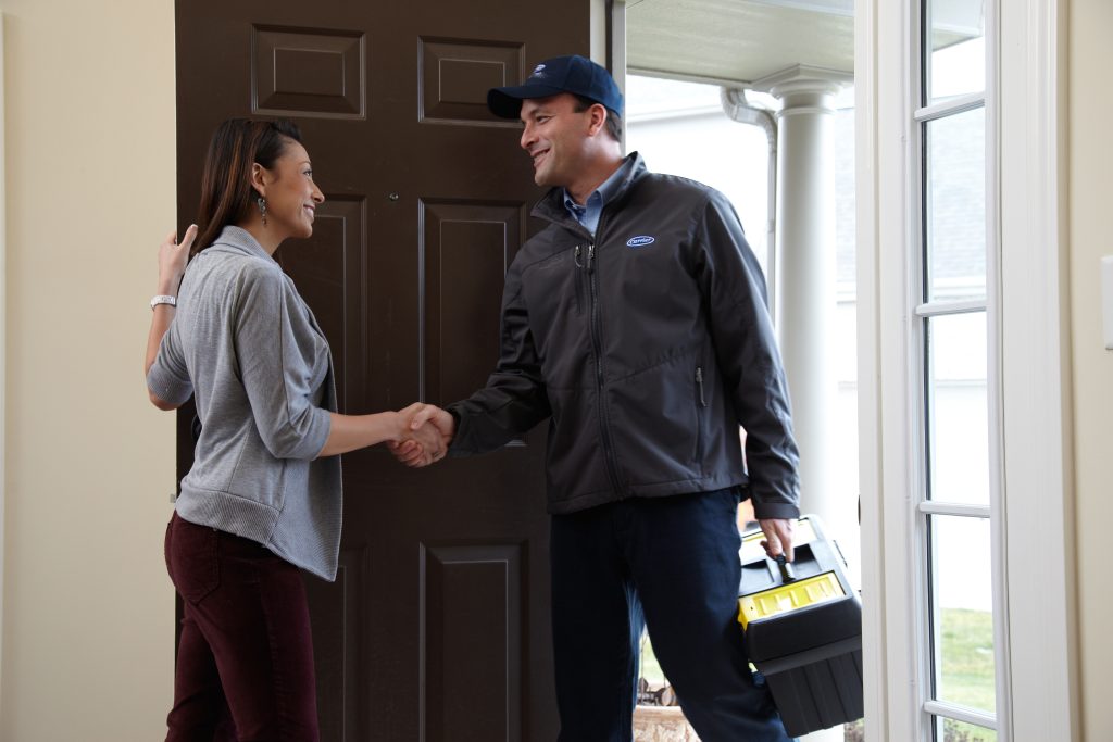 HVAC technician with a tool bag greeting a homeowner at their front door